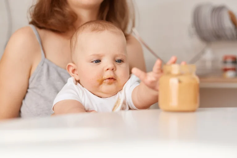 curious child stretching out arm feed jar faceless mother feeds her little infant daughter with vegetable puree sitting table home feeding up 176532 15587